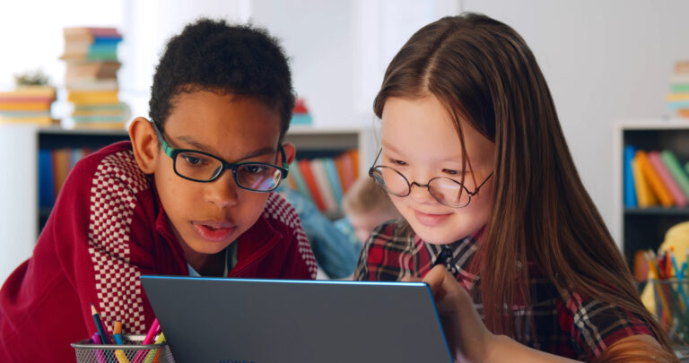 Two Preteen Diverse Students Using Laptop In Classroom